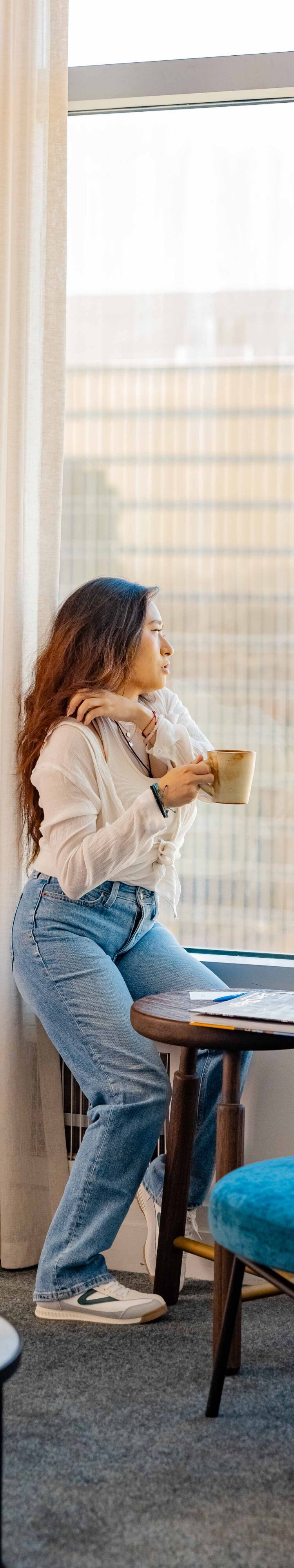 woman sitting in window holding coffee looking out