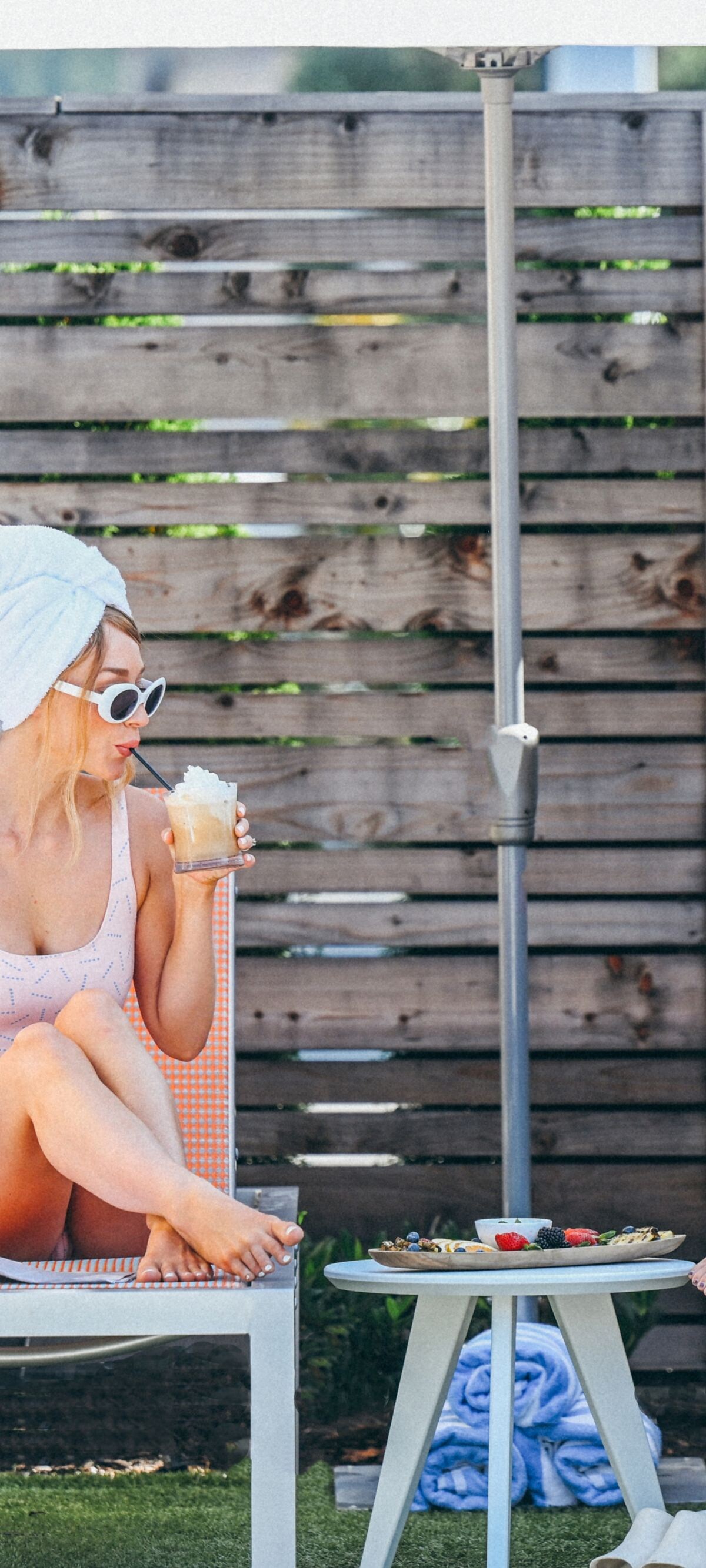 2 women sip drinks on pool chairs