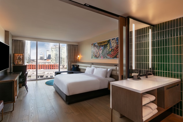 Guestroom with bathroom and bed facing city.