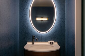 Medio baño con espejo iluminado y muro azul.