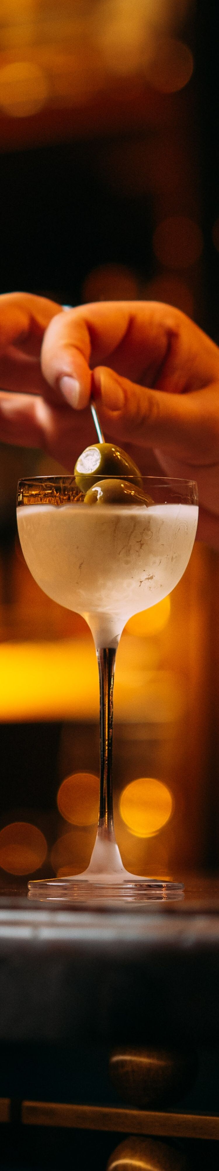 Olive skewer added to martini cocktail