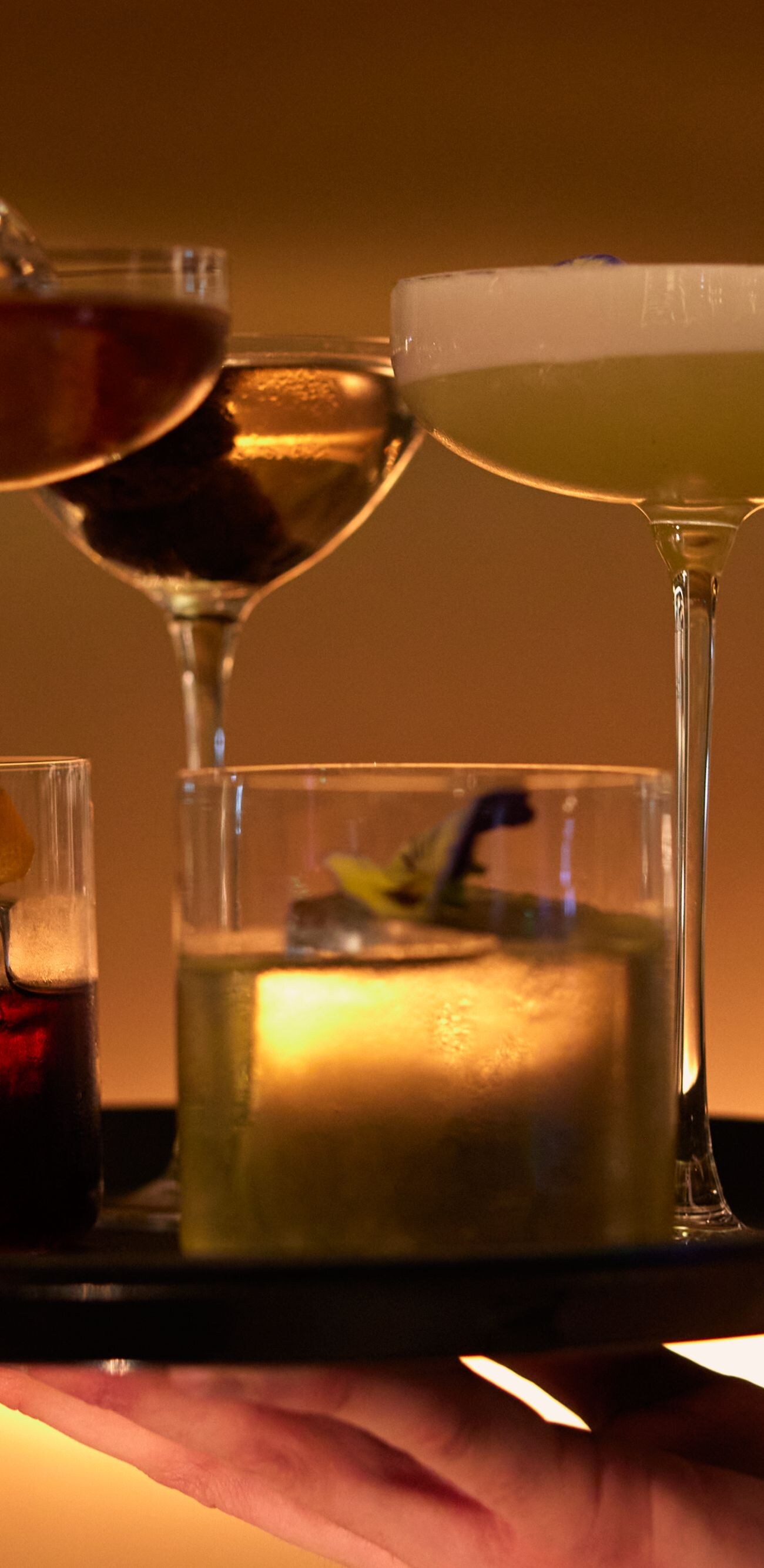 A hand holding a tray with four different cocktail