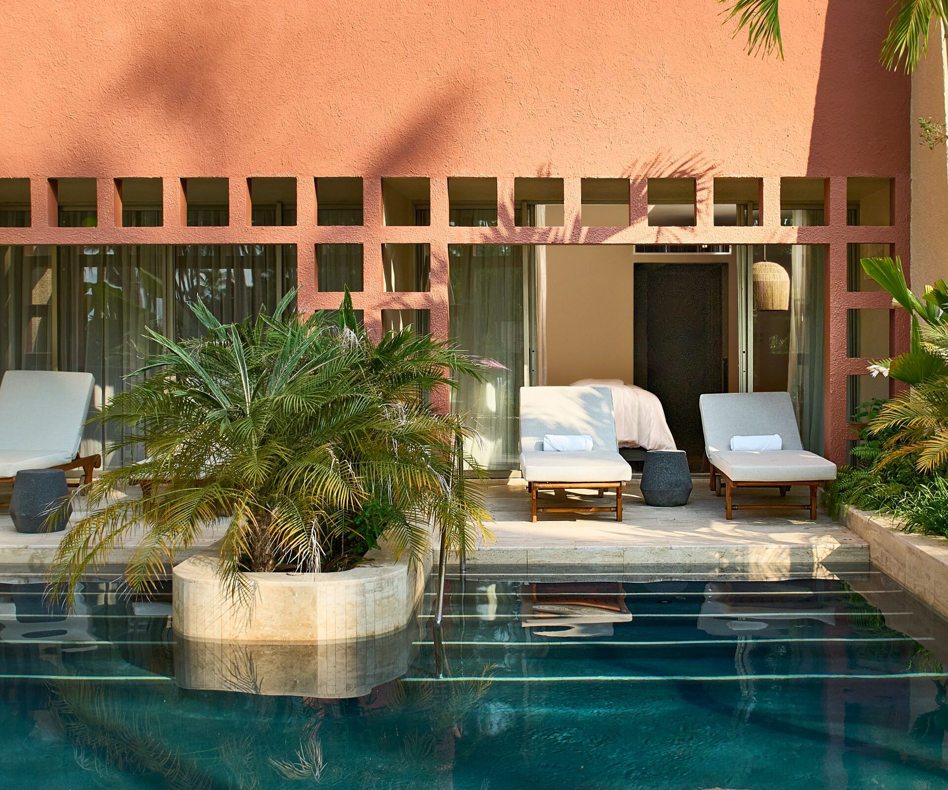 Sillas reclinables junto a la piscina con plantas tropicales y piscina