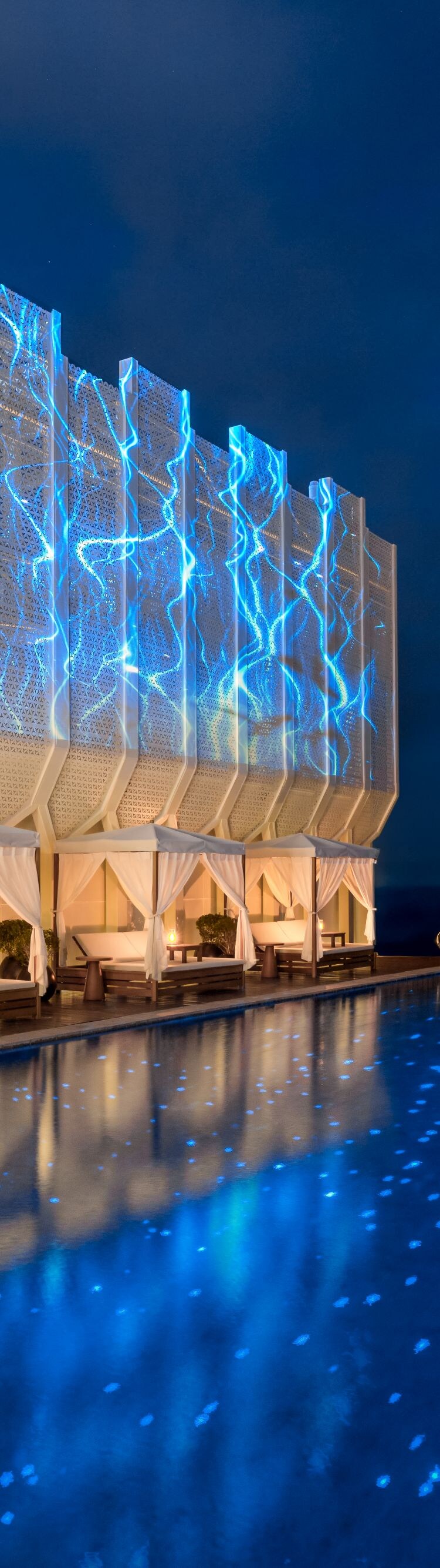 A pool with covered loungers at night.