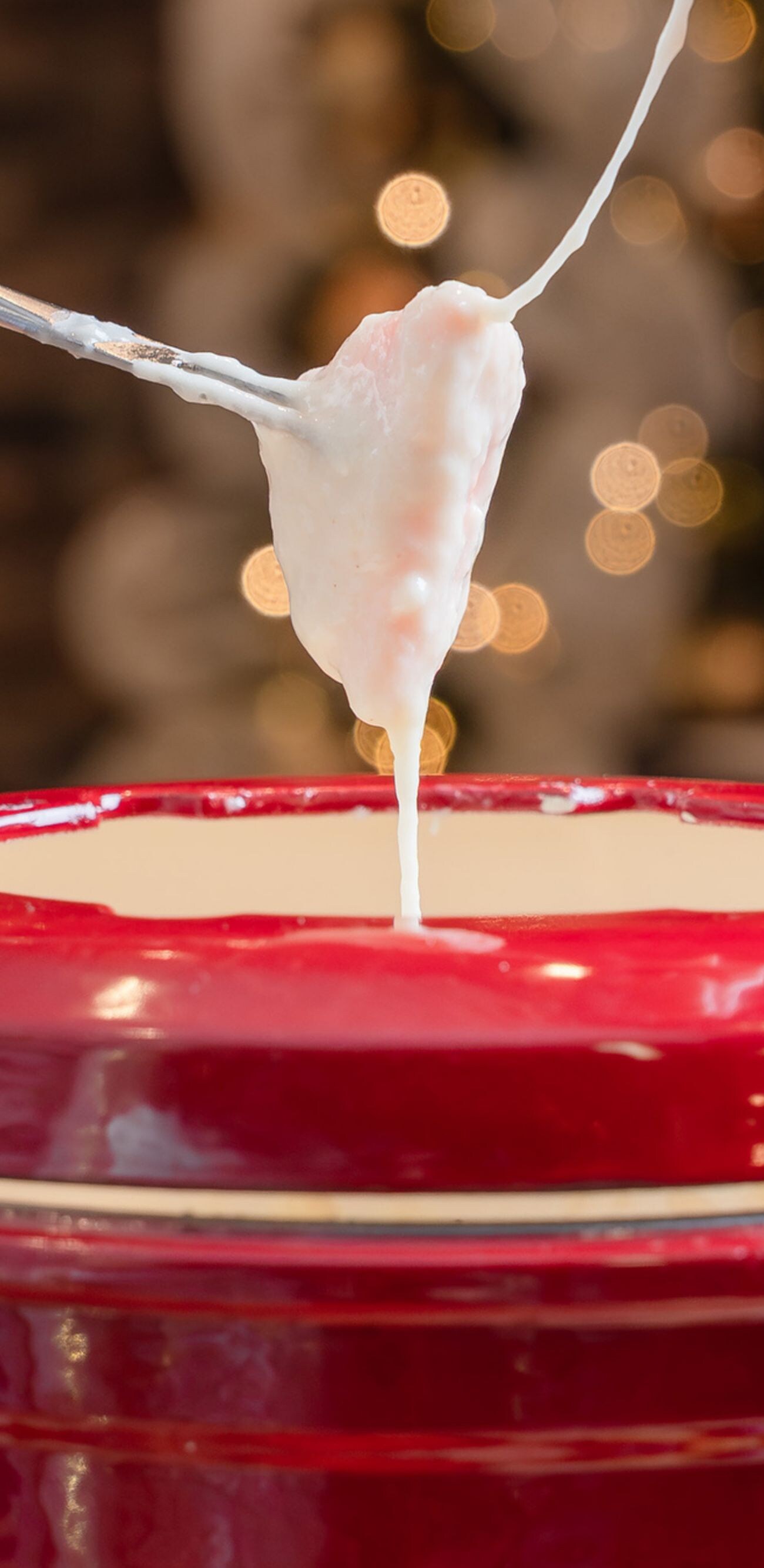 Le fromage s'étire au-dessus d'une marmite à fondue rouge.