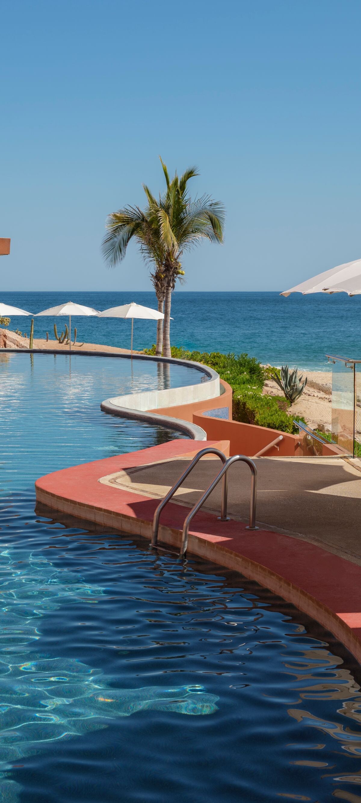 Curved beachfront pool with umbrellas and ocean 