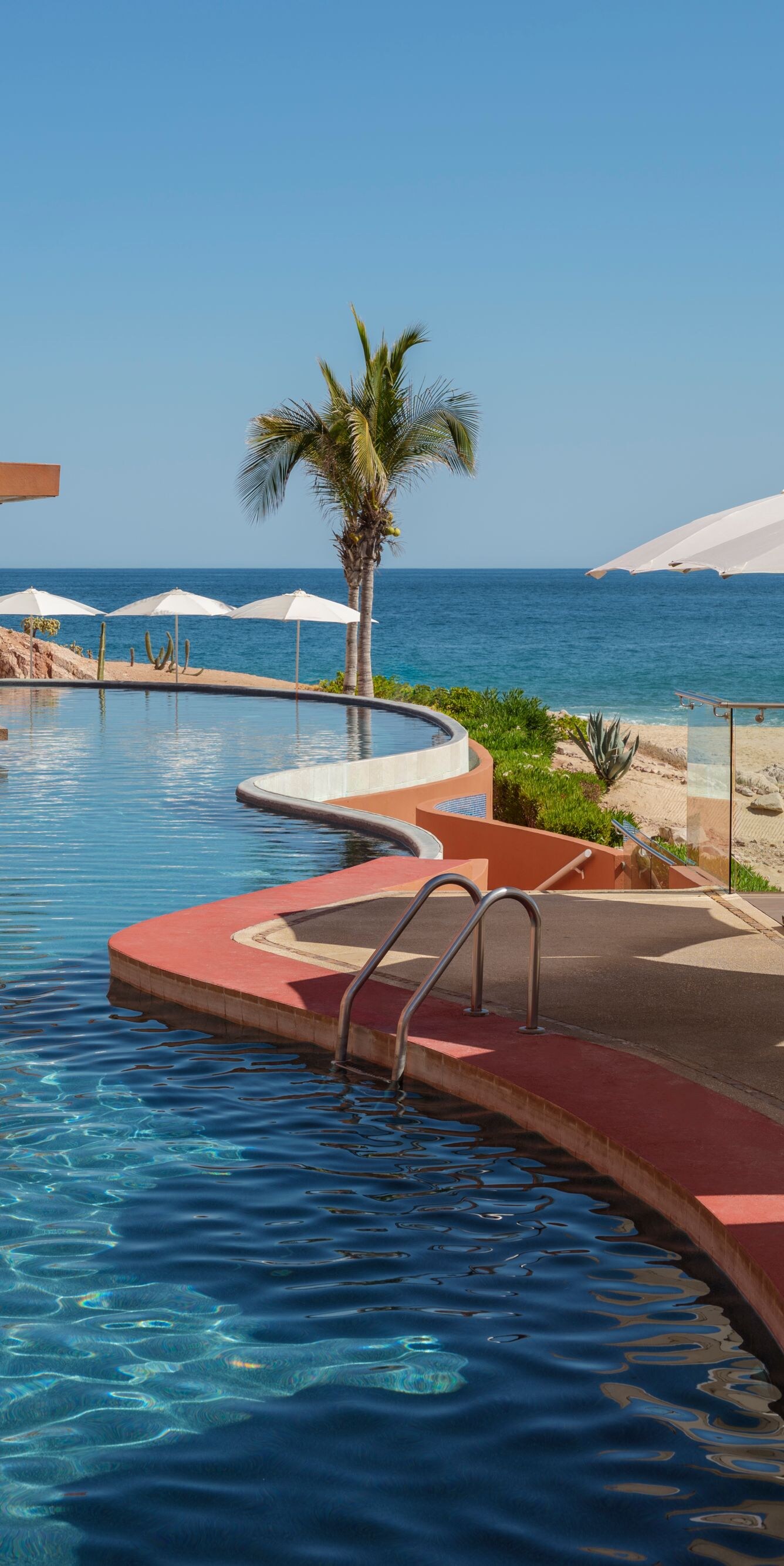 Curved beachfront pool with umbrellas and ocean 