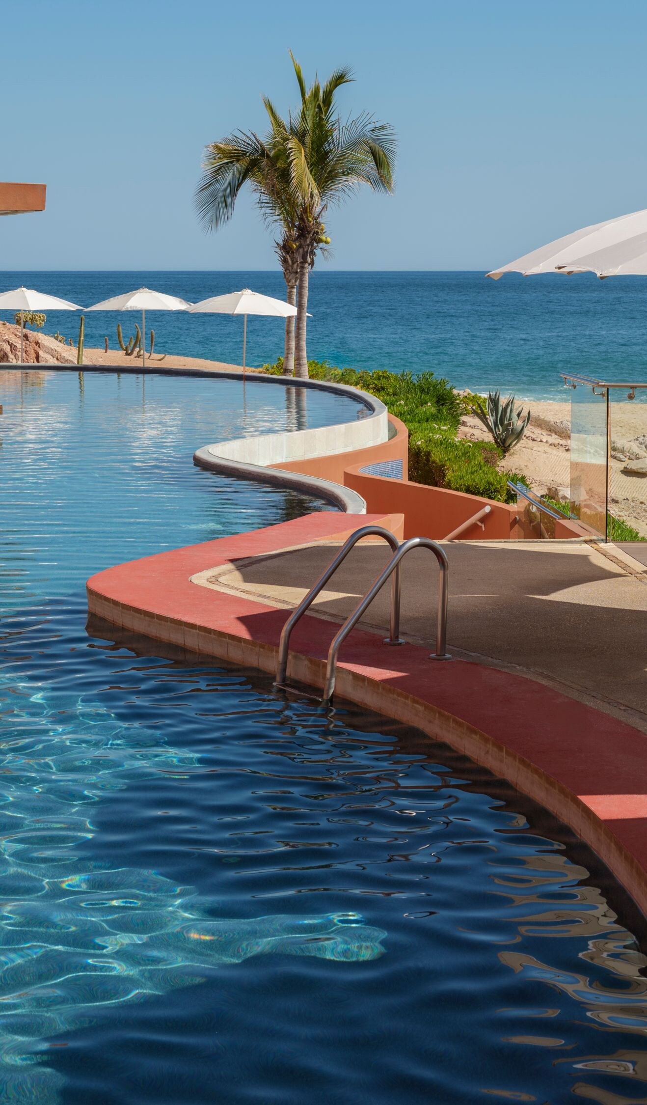 Curved beachfront pool with umbrellas and ocean 
