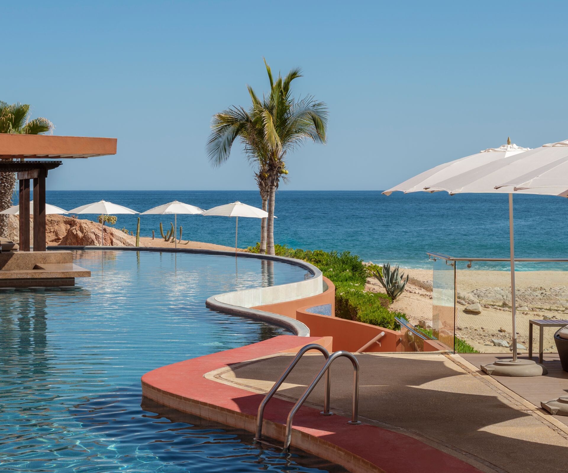 Piscina en forma curva frente al mar con sombrillas 