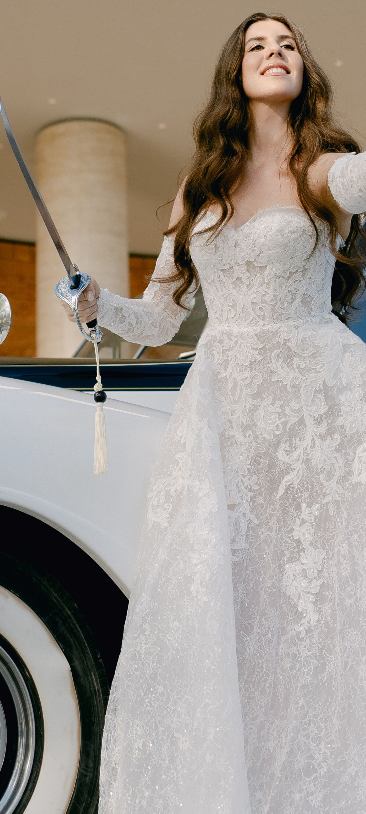 Person in wedding gown raising bottle beside car
