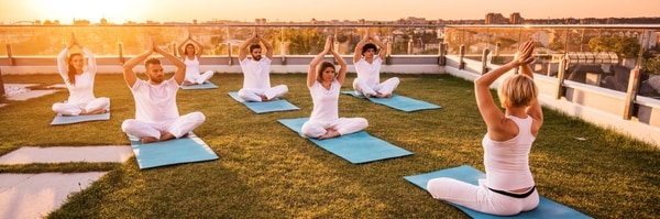 Group of people on the rooftop garden practicing yoga at sunset.
