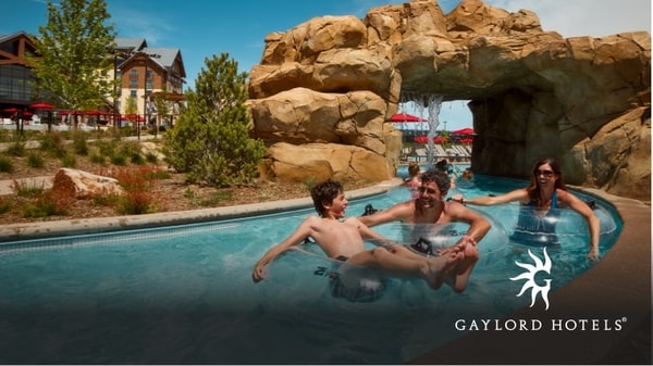 A family having fun in a water park pool with a rocky arch and a resort in the background in the lazy river at Arapahoe Springs.