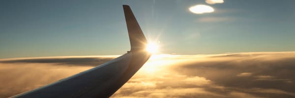 日没時の雲の上を飛行する航空機の翼