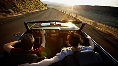 Junges Paar fährt bei Sonnenuntergang in einem Cabriolet.