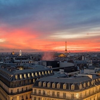 Paris skyline bathed in pink light at dusk, with the Eiffel Tower in the distance. 