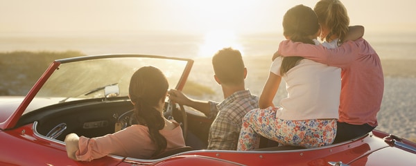 Family of four in a red convertible enjoying the sunset