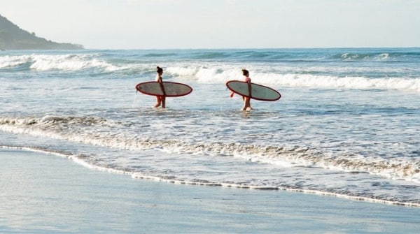 Two people walking into the ocean with surf boards
