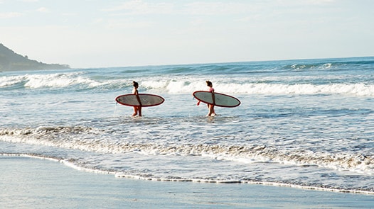Dos personas caminando hacia el océano con tablas de surf