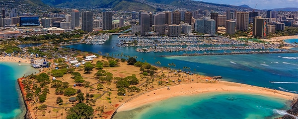 Aerial view of Ala Moana Beach in Honolulu Hawaii on a sunny day with mountains beyond.