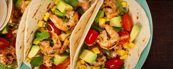 View of three grilled shrimp tacos with colorful vegetables and fresh cilantro in Los Angeles.