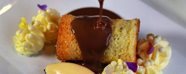 Up-close view of a modern take on a Boston cream pie being drizzled with chocolate sauce.