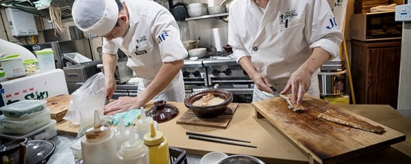 View of two chefs in Japan preparing eel in a Tokyo kitchen.