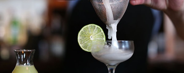 In focus view of cocktail being poured through a strain with a lime.