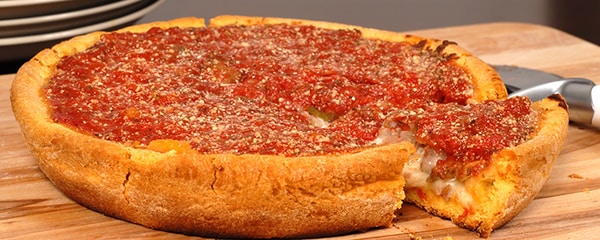 View of a Chicago deep dish pizza sitting on a large wooden cutting board.