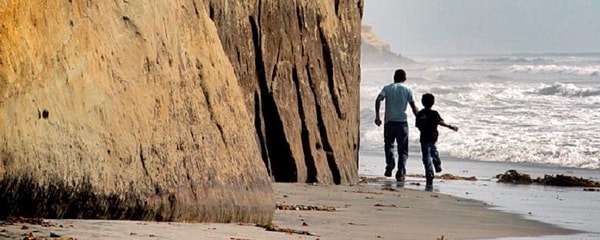 A father and sun running past cliffs in San Diego at Solana Beach.