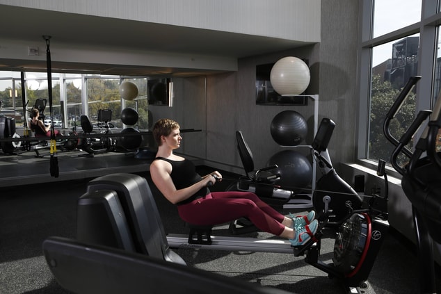 a woman on a row trainer with yoga/stretching area in the background