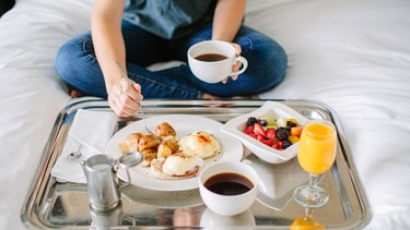    Person sitting on bed with breakfast tray  